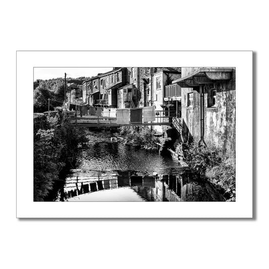 This evocative black and white art print transports you to a simpler time. Laundry drying on a clothesline, a rustic bridge, and charming cottages create a scene of peaceful village life